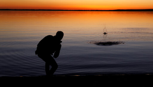 Silhouette of a man skipping stones on a lake at sunset.