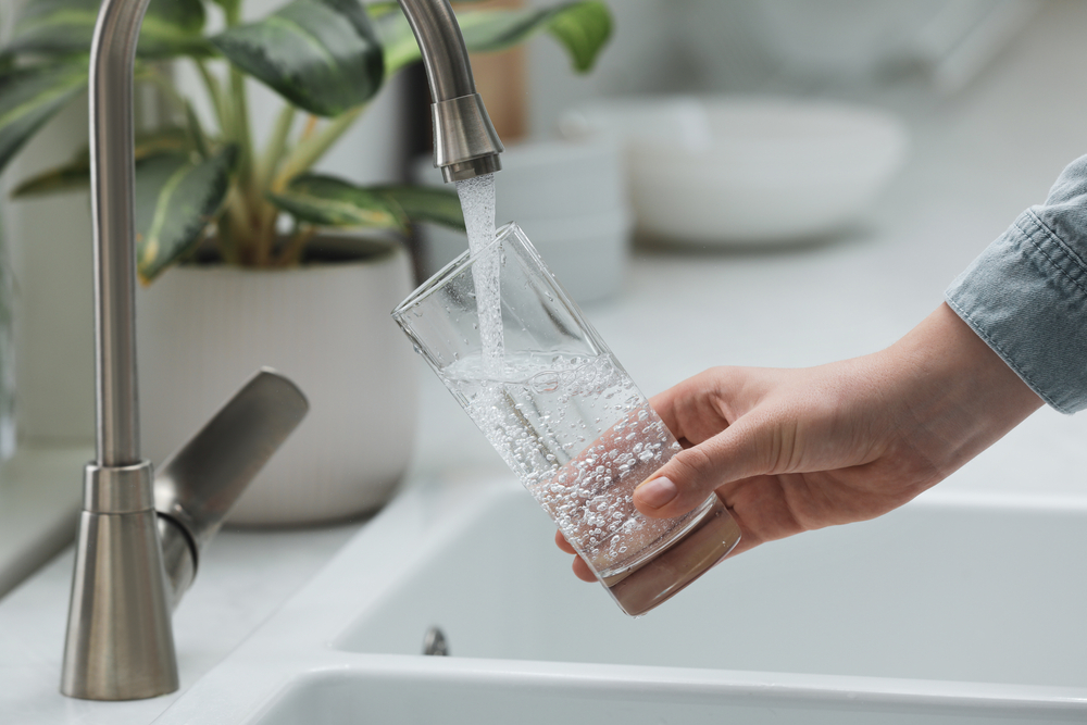 Close-up of a person filling a glass with tap water.