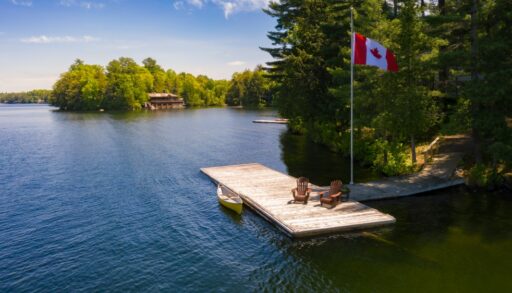Two Muskoka chairs on a dock with a Canadian flag standing next to it.