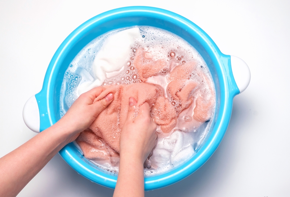 Overhead view of a person's hands as they wash clothing in a blue bucket.