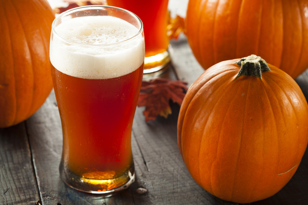 Frothy orange-coloured pumpkin beer on a table in front of a small pumpkin.