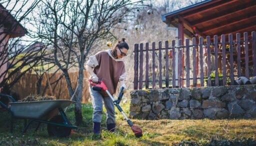 Woman using a power tool to trim grass.