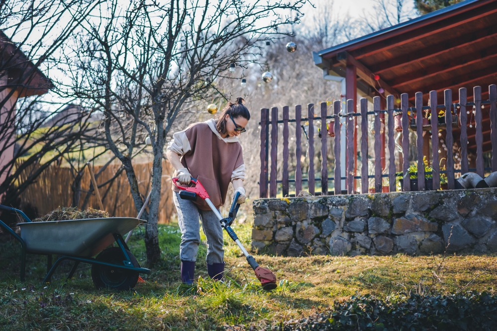 Woman using a power tool to trim grass.