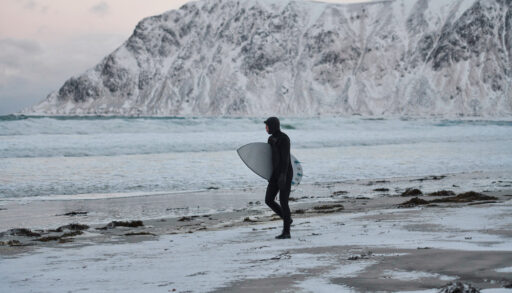 Cold water surfer carrying a surfboard and walking towards the Arctic ocean.