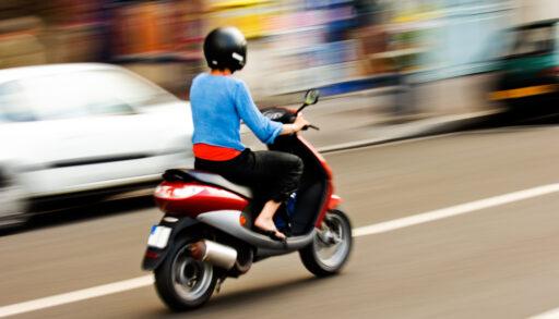 Panning shot of a person riding a moped.