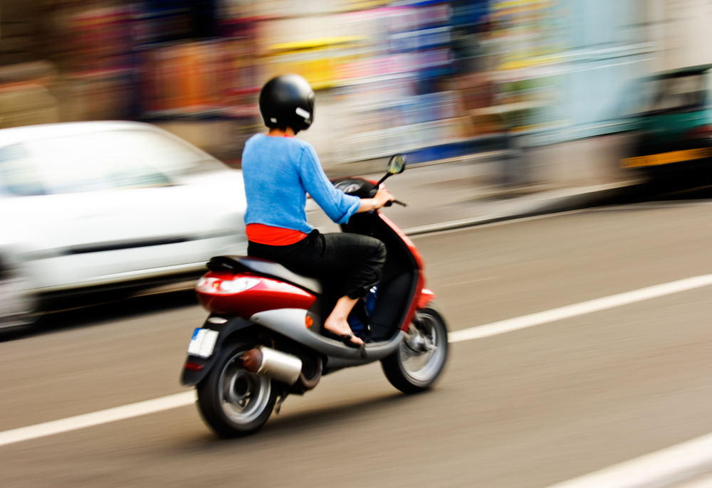 Panning shot of a person riding a moped.