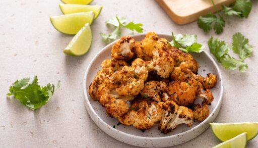 Plate of roasted cauliflower surrounded by lime wedges.