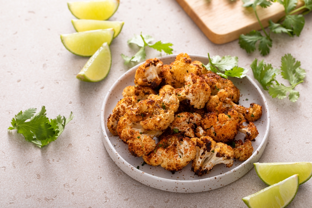 Plate of roasted cauliflower surrounded by lime wedges.