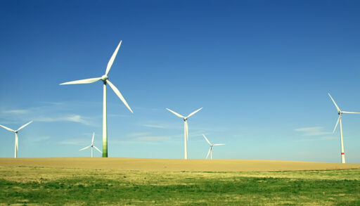Wind turbines on an empty green field with a blue sky.