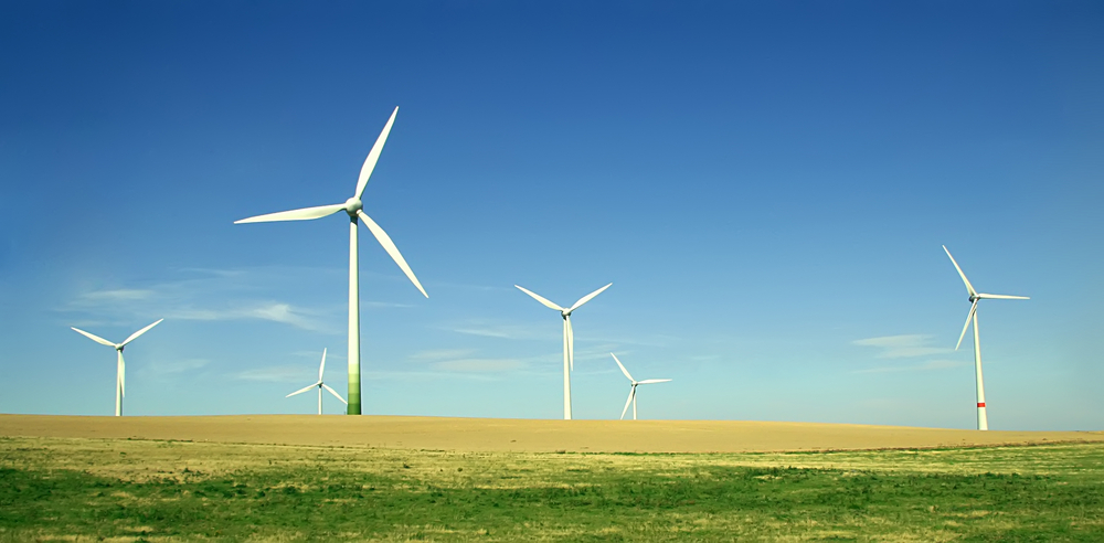 Wind turbines on an empty green field with a blue sky.