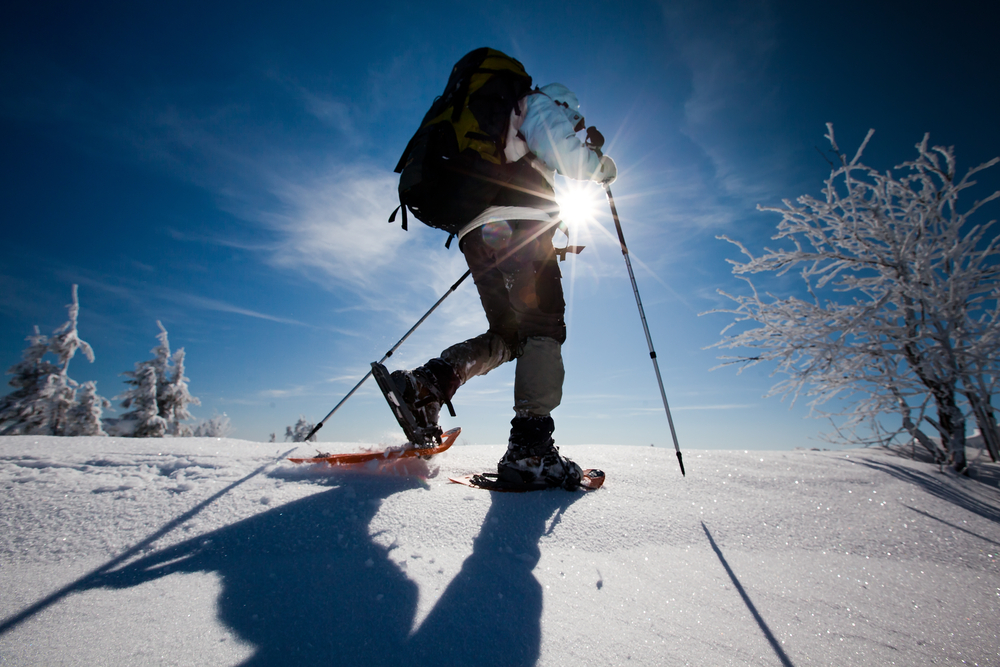 Low angle of a person wearing snowshoes and hiking in the snow, with the sun shining behind them.