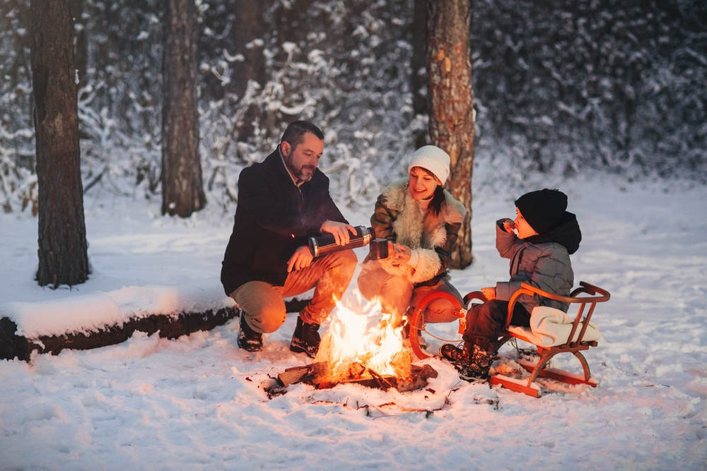 Parents and a child sitting around a winter campfire.