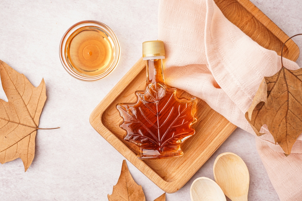 Overhead view of a bottle of maple syrup on a wooden board next to a tea towel.