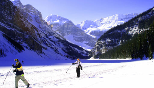 Two people cross-country skiing in a valley surrounded by mountains.