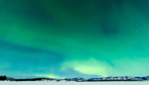 Green Northern Lights over mountains and a snowy landscape in Lake Laberge, Yukon.