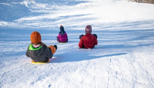 Three children tobogganing down a snowy hill.