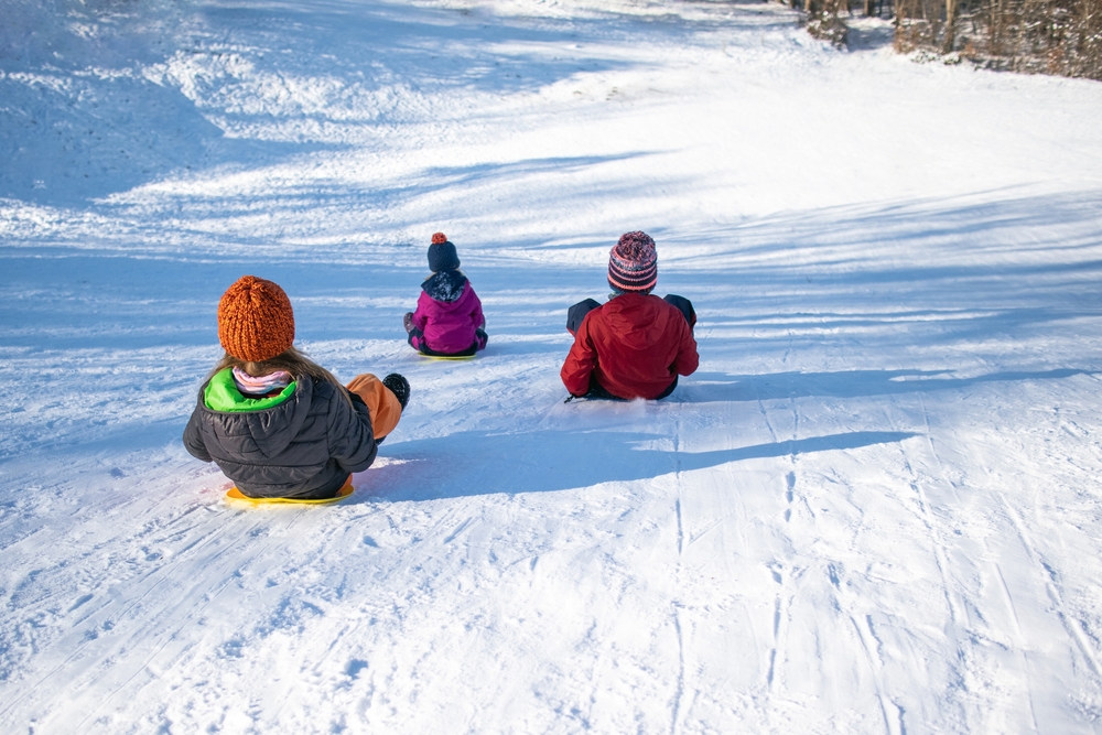 Three children tobogganing down a snowy hill.