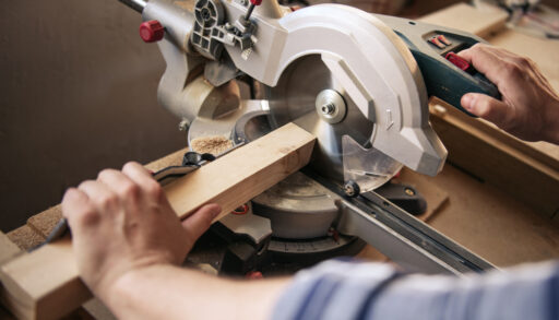 Close-up of a man using a mitre saw to cut a piece of wood.