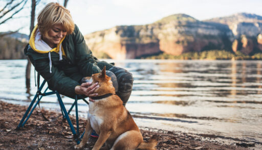 Young woman sitting next to a lake petting a dog.