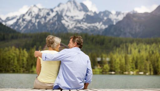 Retired couple sitting on a dock with mountains in the background.