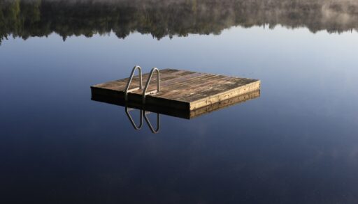 A wooden dock on a still lake with a reflection of the surrounding trees.