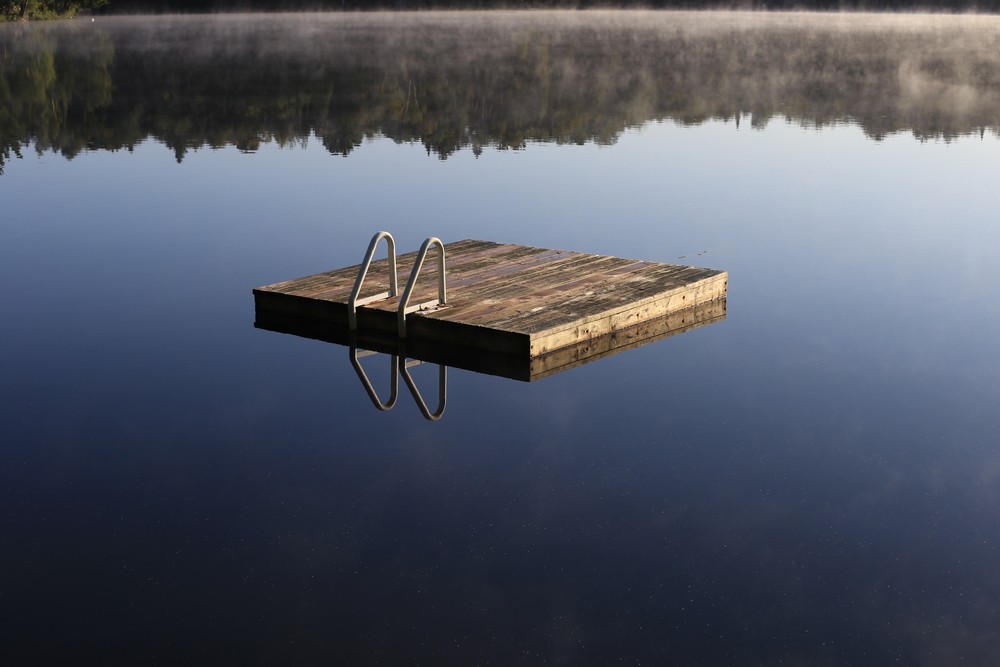 A wooden dock on a still lake with a reflection of the surrounding trees.