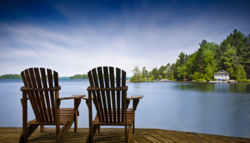 Two Muskoka chairs on a dock overlooking a lake.