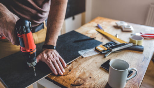 Close-up of a man drilling a hole in a piece of wood.