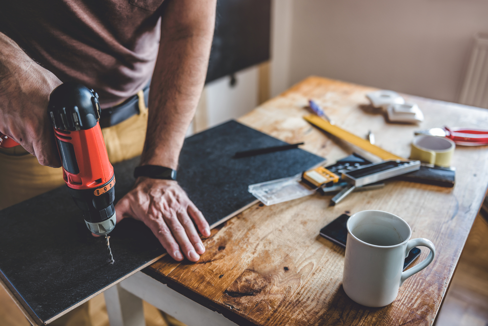 Close-up of a man drilling a hole in a piece of wood.
