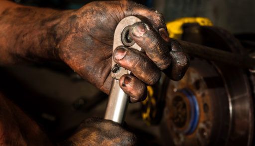 Close-up of a man's hands covered in oil as they work to repair an engine.