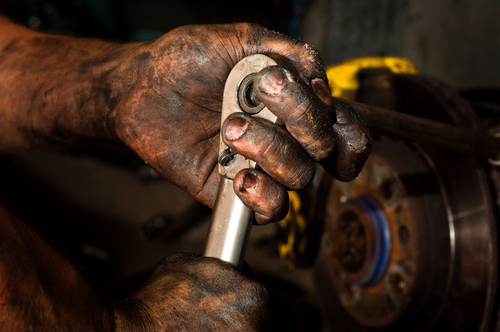 Close-up of a man's hands covered in oil as they work to repair an engine.
