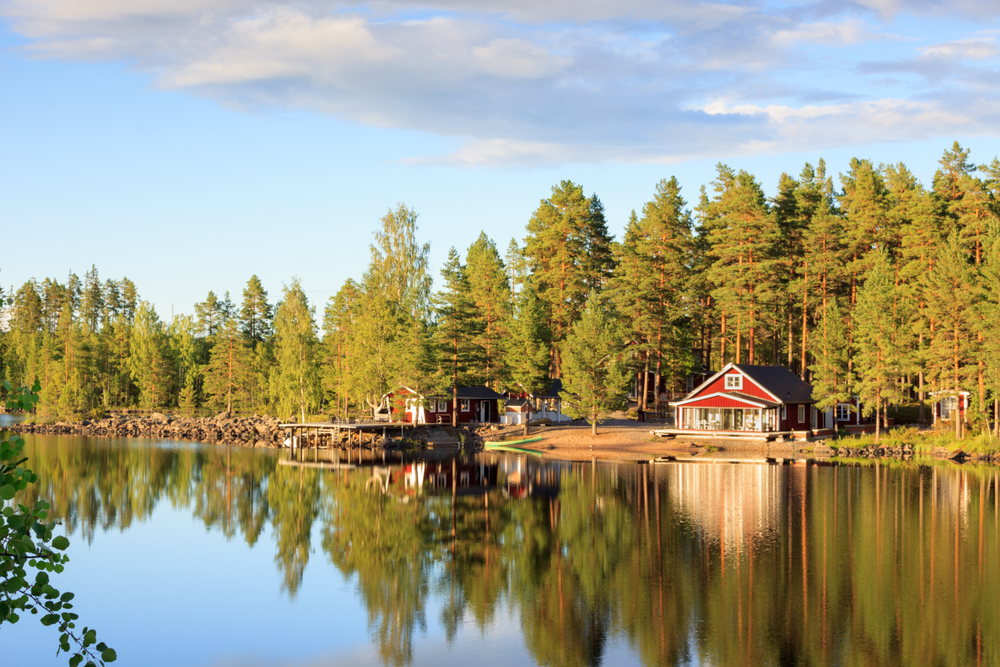 Traditional red cottage on a lake surrounded by trees.