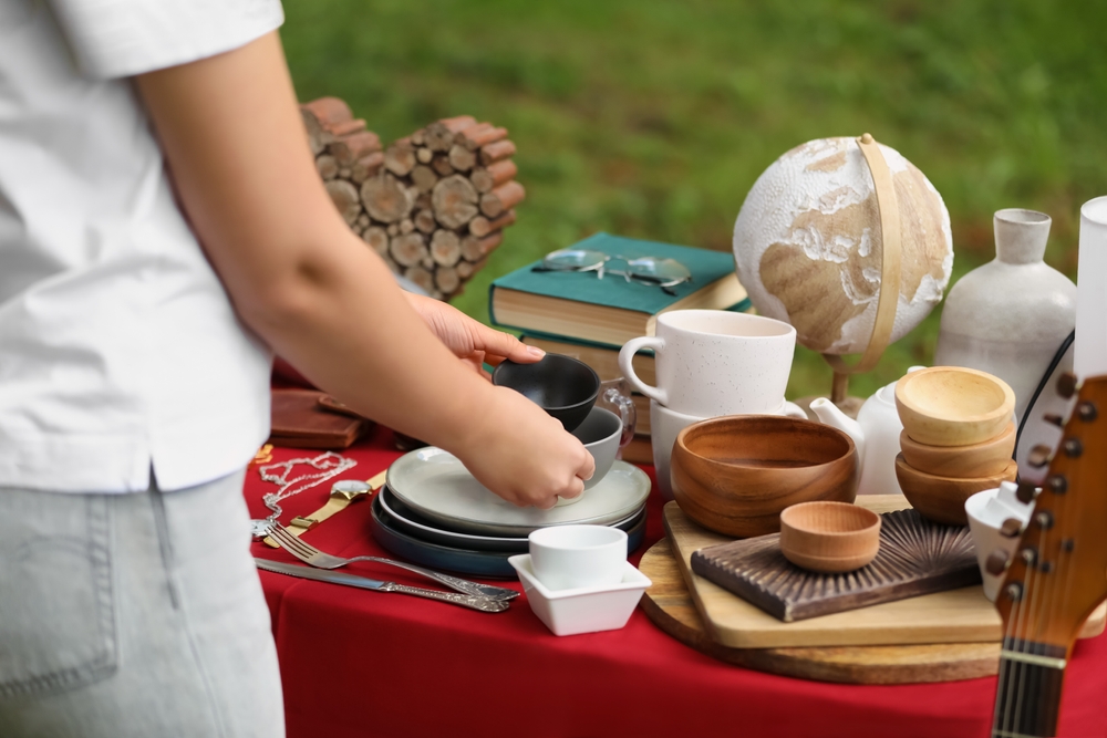 Close-up of a woman picking up dishes off a table at a yard sale.