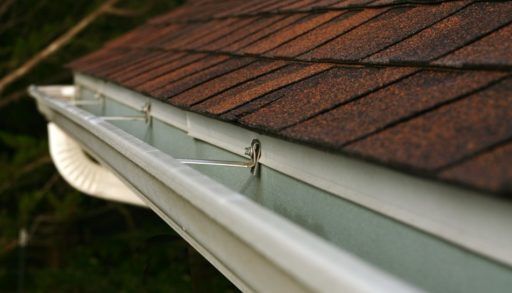 Close-up of a white eavestrough attached to a brown roof.