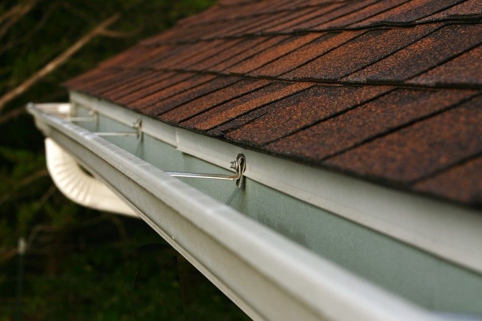 Close-up of a white eavestrough attached to a brown roof.