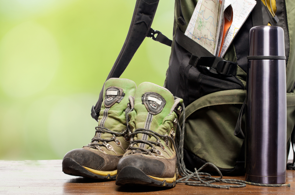Close-up of outdoor equipment like hiking boots, a backpack and a water bottle.