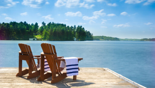 Two Muskoka chairs on a dock with white and blue beach towels.