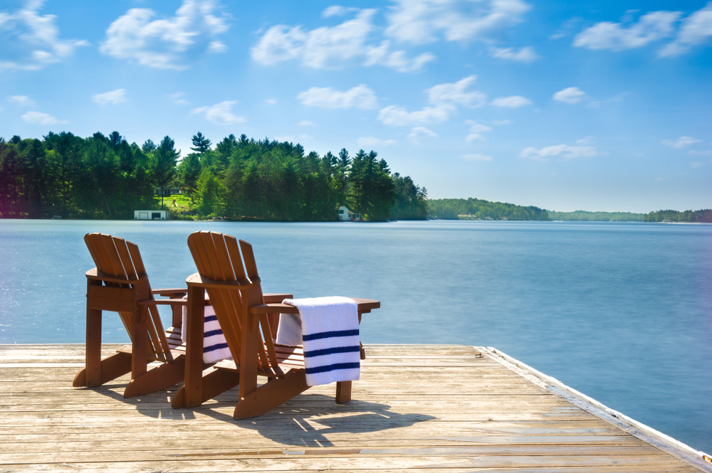 Two Muskoka chairs on a dock with white and blue beach towels.