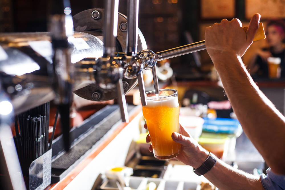 Close-up of a bartender's hands as they pour beer into a glass.