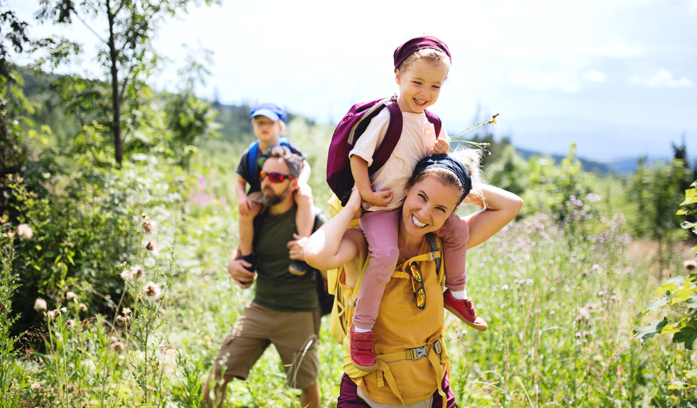 Family hiking in a field, with a woman carrying a kid on her shoulders.