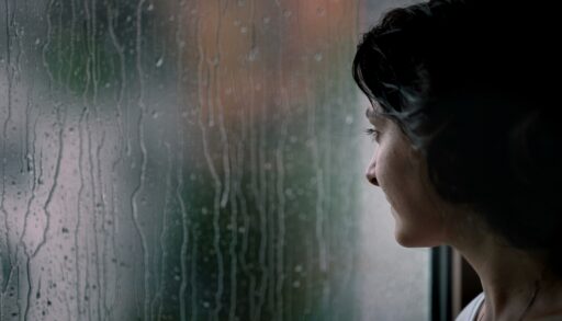 Young woman looking out a rain-covered window.