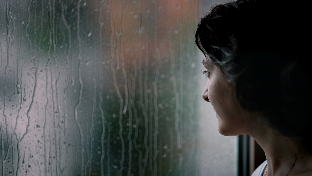 Young woman looking out a rain-covered window.