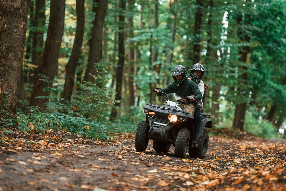 Two people riding an ATV on a footpath in a forest.