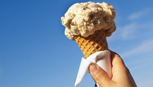 Person holding a vanilla ice cream cone in front of a blue sky.