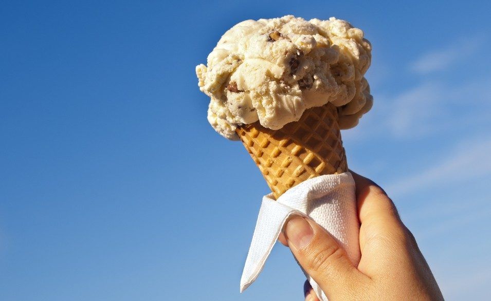 Person holding a vanilla ice cream cone in front of a blue sky.