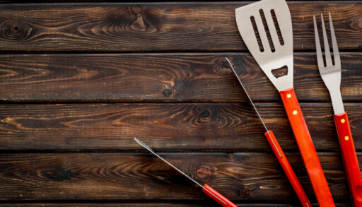 A red spatula, grill fork and tongs on a wooden background.