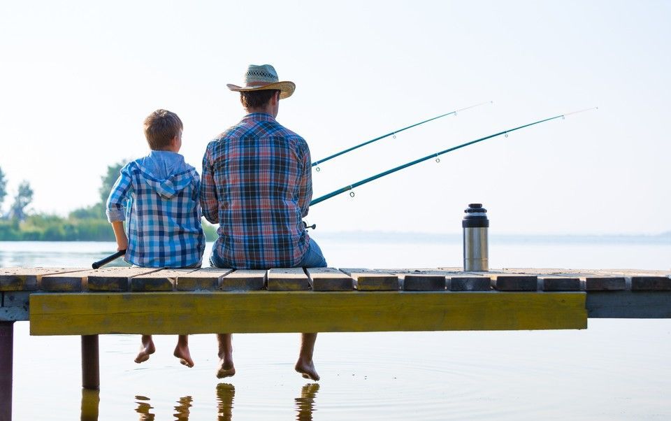 Father and son sitting on a wooden dock fishing.