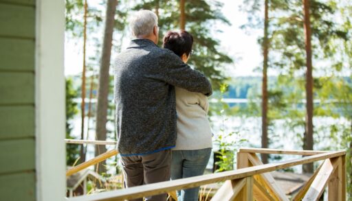 Older couple standing on a cottage deck looking out at a lake.
