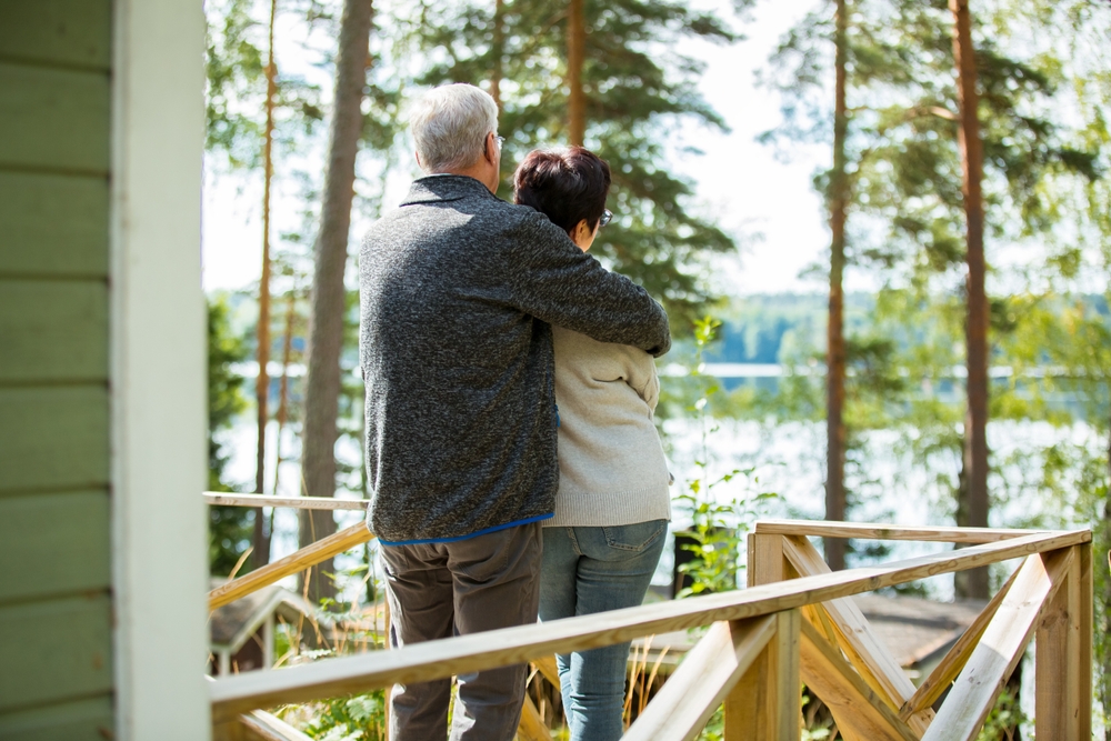 Older couple standing on a cottage deck looking out at a lake.