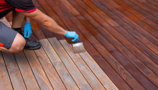 Close-up of a person applying a dark stain to a deck.